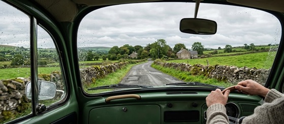 A car driving through lush green rolling hills under a cloudy sky