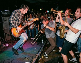 A punk rock band performing on stage with a trombone player