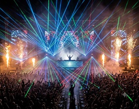 A DJ performing at a massive music festival with laser lights